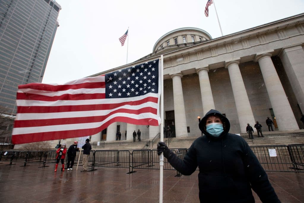 Una persona sostiene una bandera estadounidense frente al Capitolio Estatal de Ohio en Columbus, Ohio, el 17 de enero de 2021. (Foto de STEPHEN ZENNER/AFP vía Getty Images)