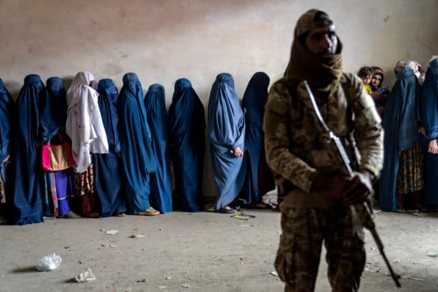 Un combatiente talibán monta guardia mientras unas mujeres esperan para recibir raciones de comida distribuidas por un grupo de ayuda humanitaria en Kabul, Afganistán, el 23 de mayo de 2023. (Ebrahim Noroozi/AP)