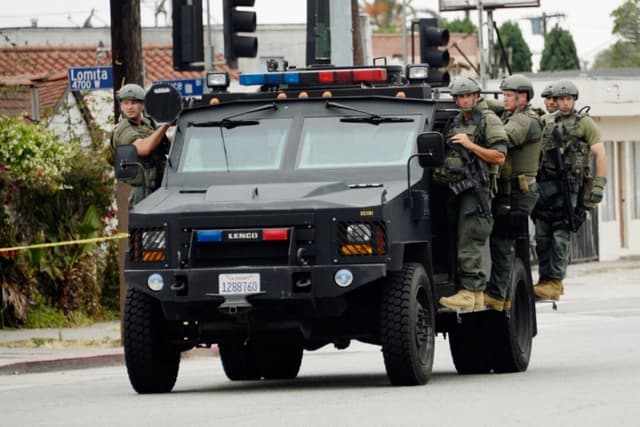 Miembros del equipo SWAT del Sheriff del Condado de Los Ángeles, de pie sobre un vehículo blindado, llegan para ayudar a los oficiales del Departamento de Policía de Los Ángeles durante una búsqueda masiva de un sospechoso que intentó matar a dos detectives, en Los Ángeles, el 25 de junio de 2013. (Kevork Djansezian/Getty Images)
