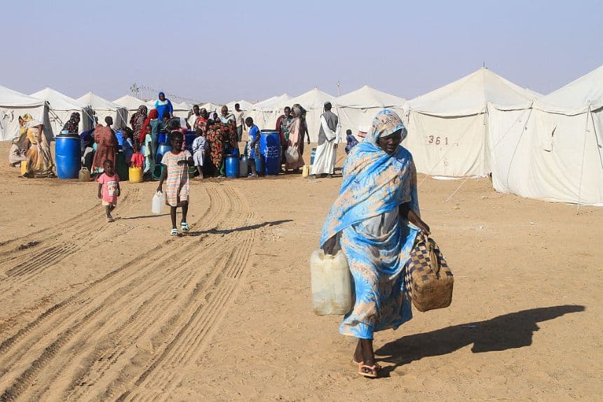 Una mujer sudanesa que huyó de El-Fasher, en Darfur, transporta bidones de agua en el campamento de Al-Afad para personas desplazadas en la ciudad de Al-Dabba, en el norte de Sudán, el 21 de noviembre de 2025. (EBRAHIM HAMID/AFP a través de Getty Images)