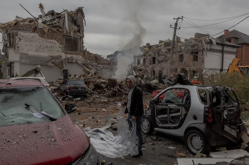 Un hombre se prepara para cubrir un coche dañado con una lámina de plástico en el lugar donde se encuentran edificios residenciales gravemente dañados tras un ataque aéreo ruso en las afueras de Kiev, el 28 de septiembre de 2025. (Roman PILIPEY / AFP vía Getty Images)