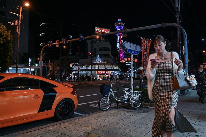 Una mujer (derecha) caminando por la calle con la Torre Tsutenkaku (detrás del centro) al fondo, en la popular zona turística de Shinsekai, en el barrio de Naniwa, Osaka, el 29 de septiembre de 2025. (RICHARD A. BROOKS/AFP vía Getty Images)