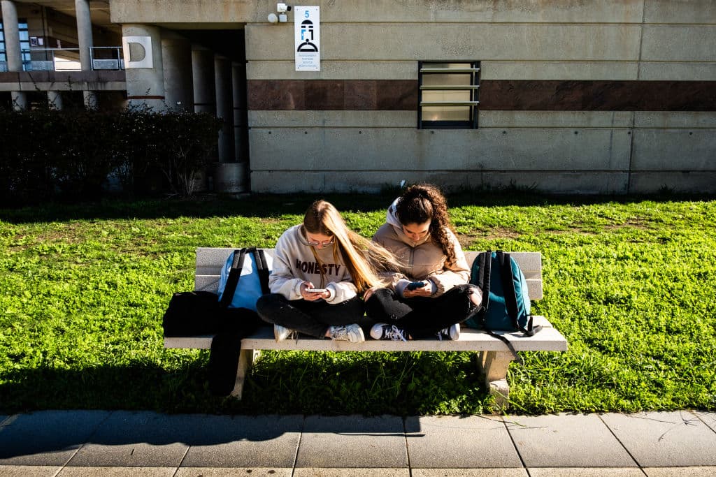 Jóvenes adolescentes y estudiantes de secundaria sentadas en un banco durante el recreo del instituto y consultando sus teléfonos o smartphones y redes sociales una al lado de la otra en el Lycee Aristide Maillol de Perpiñán, en el departamento de Pirineos Orientales, en el sur de Francia, el 14 de noviembre de 2024. (JC MILHET/Hans Lucas/AFP vía Getty Images)