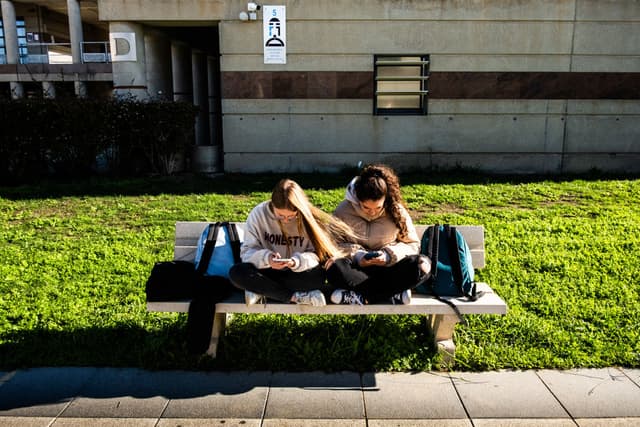 Jóvenes adolescentes y estudiantes de secundaria sentadas en un banco durante el recreo del instituto y consultando sus teléfonos o smartphones y redes sociales una al lado de la otra en el Lycee Aristide Maillol de Perpiñán, en el departamento de Pirineos Orientales, en el sur de Francia, el 14 de noviembre de 2024. (JC MILHET/Hans Lucas/AFP vía Getty Images)