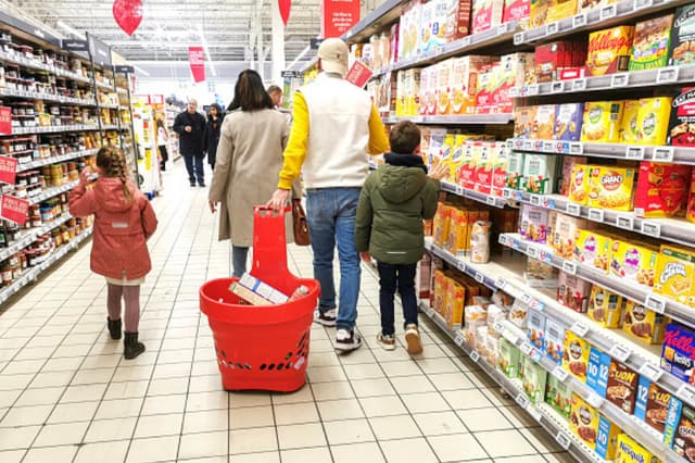 Dos padres y sus dos hijos caminan por una sección de pasteles, galletas y mermeladas, con el padre tirando de una cesta llena de artículos, en el supermercado Auchan de Guilherand Granges, Francia, el 1 de febrero de 2025. (Nicolas Guyonnet / Hans Lucas/AFP vía Getty Images)