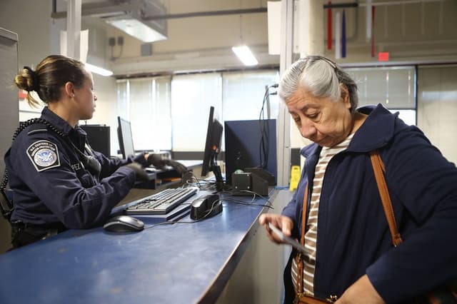 Una oficial de Aduanas y Protección Fronteriza de los Estados Unidos espera a un migrante después de revisar los documentos de una mujer que ingresa a Estados Unidos por el puerto de entrada de San Ysidro el 9 de abril de 2018 en San Ysidro, California. (Mario Tama/Getty Images)