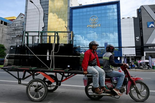 Trabajadores en su carreta cargada de vidrio pasan frente a una sucursal del Prince Bank, en Phnom Penh, el 15 de octubre de 2025. (TANG CHHIN SOTHY/AFP vía Getty Images)