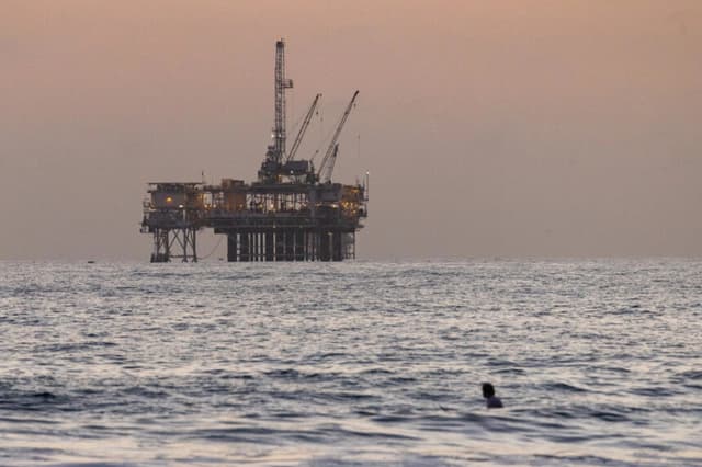 Una plataforma petrolífera se divisa al fondo, detrás de unos surfistas en Huntington Beach, California, el 12 de septiembre de 2024.