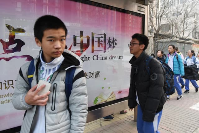 Jóvenes pasan frente a una valla publicitaria sobre el "sueño chino", un eslogan asociado al líder chino Xi Jinping, frente a una escuela en Beijing el 12 de marzo de 2018. (Greg Baker/AFP vía Getty Images)