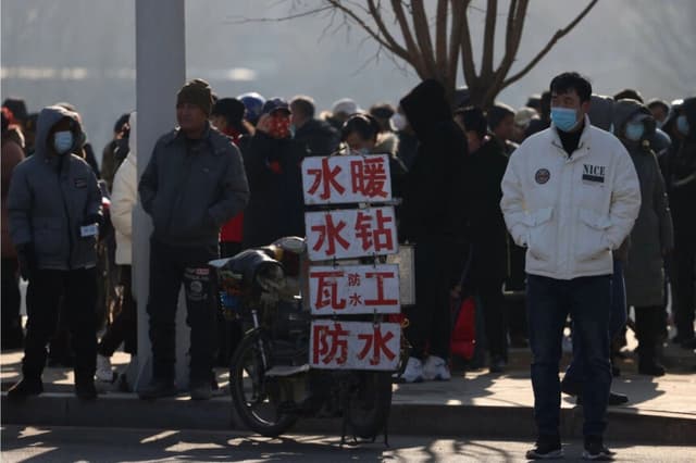 os trabajadores migrantes se encuentran cerca de carteles que anuncian sus habilidades mientras esperan en una calle para ser contratados en Shenyang, en la provincia nororiental de Liaoning, China, en esta foto de archivo. (AFP vía Getty Images)