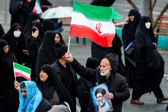 Un doliente sostiene una bandera iraní y una fotografía del líder iraní asesinado, el ayatolá Alí Jamenei, mientras marcha junto a otras personas durante la ceremonia fúnebre del ministro de Inteligencia iraní asesinado, Esmail Khatib, y su familia, tras la oración musulmana semanal del viernes al mediodía en Teherán, el 20 de marzo de 2026. El ejército israelí declaró el 18 de marzo que no detendría su "serie de eliminaciones" de altos cargos iraníes, tras anunciar que había matado a Khatib. (AFP vía Getty Images).