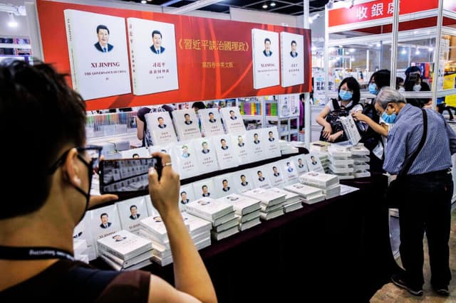 Una mujer (izquierda) toma una foto de un libro escrito por el presidente chino Xi Jinping sobre gobernanza en una feria del libro en Hong Kong el 21 de julio de 2022. (Foto de ISAAC LAWRENCE/AFP vía Getty Images)