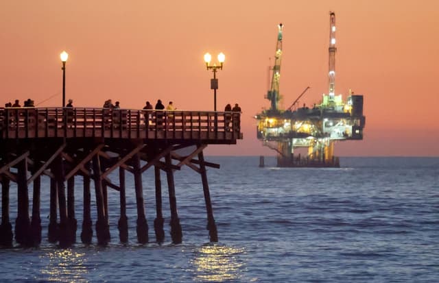 Varias personas se encuentran en un muelle con la plataforma petrolífera y de gas Esther a la distancia en Seal Beach, California, el 5 de enero de 2025. (Mario Tama/Getty Images)