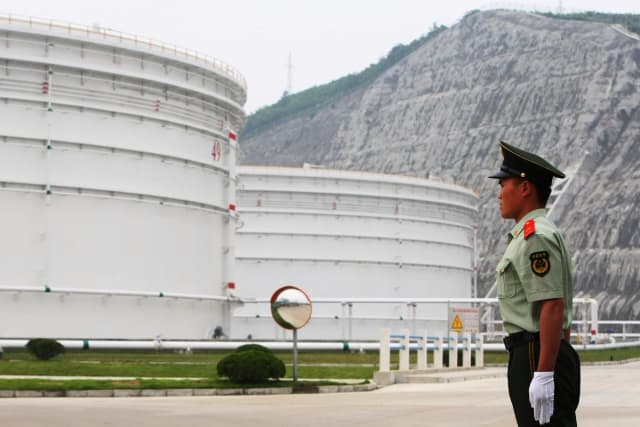 Un guardia de seguridad permanece de pie cerca de grandes tanques de petróleo en la Base Nacional de Reservas Petroleras de Zhenghai, en Ningbo, provincia de Zhejiang, China, el 3 de junio de 2009. (Feng Li/Getty Images)