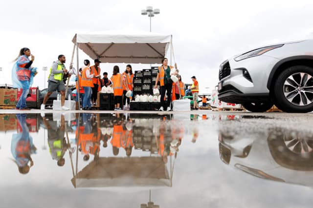 Los voluntarios reparten leche y otros alimentos bajo la lluvia mientras la gente llega en sus vehículos para recibir ayuda alimentaria en un reparto de pavos destinado a los trabajadores federales y a los beneficiarios del Programa de Asistencia Nutricional Suplementaria (SNAP), organizado por el Banco de Alimentos de Houston en Houston, Texas, el 22 de noviembre de 2025. Según los organizadores, se atendió a más de 3500 familias durante el reparto de alimentos. (Mark Felix / AFP vía Getty Images).