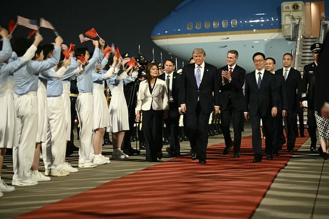 El presidente de EE. UU., Donald Trump (C), y el embajador de EE. UU. en China, David Perdue (centro-D), escoltados por el vicepresidente de China, Han Zheng (D), son recibidos por jóvenes chinos a su llegada al Aeropuerto de Beijing, el 13 de mayo de 2026. (Foto de Brendan SMIALOWSKI / AFP vía Getty Images)
