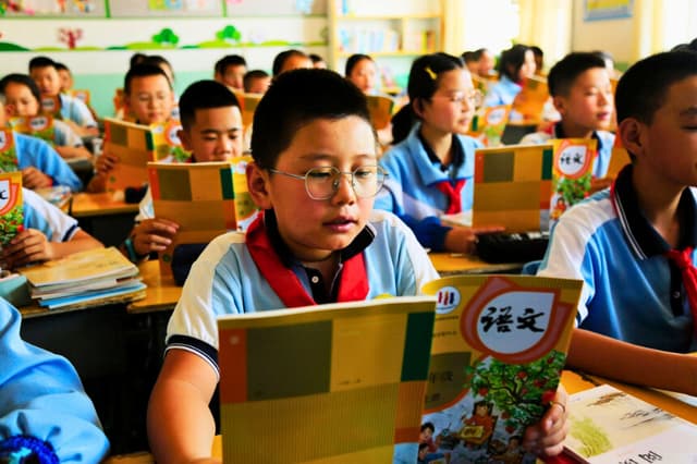Unos alumnos leen sus libros de texto en una escuela primaria de la ciudad de Zhangye, en la provincia de Gansu, China, el 28 de agosto de 2023. (STR/AFP vía Getty Images).