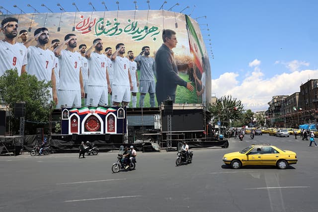 Enorme valla publicitaria de la selección nacional de fútbol de Irán en la próxima Copa Mundial de 2026, instalada en un edificio en la plaza Enghelab de Teherán el 18 de mayo de 2026. La selección nacional de fútbol de Irán se dirigía a Turquía ese mismo día para disputar un último partido amistoso y solicitar visados para viajar a Estados Unidos para la Copa Mundial de 2026, según informaron medios iraníes. (AFP vía Getty Images)