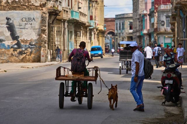 Un hombre va en triciclo con su perro atado con una correa corriendo a su lado durante un apagón en La Habana, Cuba, el 16 de marzo de 2026. (Ramón Espinosa/AP Photo).