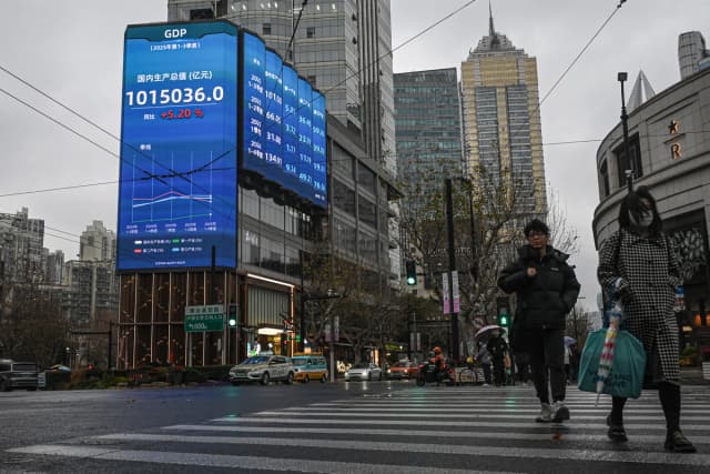 Varias personas pasan junto a una pantalla que muestra cifras del producto interior bruto en una calle de Shanghái el 19 de enero de 2026. (Jade Gao / AFP vía Getty Images).