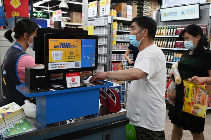Un hombre toma un recibo en una caja registradora donde se ve un letrero que indica que se acepta el pago con la nueva moneda digital de China, en una tienda Walmart en Pekín, el 2 de julio de 2021. (Foto de Greg Baker / AFP) (GREG BAKER/AFP vía Getty Images).