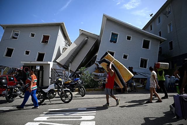 Un hombre carga un colchón frente a edificios residenciales dañados tras un terremoto en Catia La Mar, estado La Guaira, al noroeste de Caracas, el 25 de junio de 2026. El doble terremoto, el mayor registrado en Venezuela en más de un siglo, destruyó varios edificios cerca de la capital, mientras los residentes buscaban a sus familiares desaparecidos. (Federico PARRA / AFP vía Getty Images)