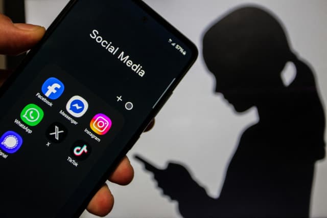 Una imagen en primer plano de una mano sosteniendo un teléfono inteligente que muestra aplicaciones de redes sociales, sobre un fondo que presenta la silueta de una niña al estilo de marionetas de sombras chinas sosteniendo un teléfono, en Túnez, Túnez, el 20 de junio de 2026. (Imen Ben Youssef/Hans Lucas/AFP vía Getty Images)