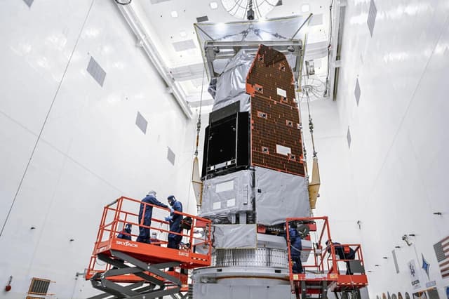 El 26 de junio de 2026, técnicos e ingenieros dentro de la Instalación de Mantenimiento de Cargas Útiles Peligrosas del Centro Espacial Kennedy de la NASA, en Florida, utilizan una grúa para elevar el Telescopio Espacial Nancy Grace Roman de la agencia hasta un soporte de trabajo especializado. (Cortesía de la NASA).