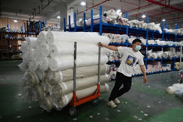 Un trabajador transporta rollos de tela tras descargarlos en un almacén de un parque industrial textil en Shaoxing, provincia de Zhejiang, China, el 9 de mayo de 2025. (Greg Baker/AFP vía Getty Images)